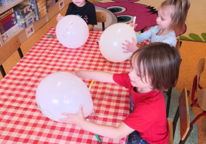 dzieci przy stolikach malują pisakami balony